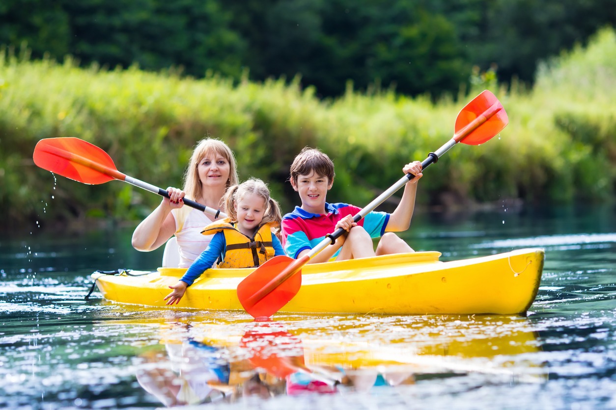 Happy family with two kids enjoying kayak ride on beautiful river. Mother with little girl and teenager boy kayaking on hot summer day. Water sport fun. Canoe and boat for children