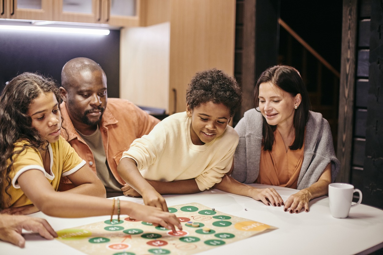 Happy parents sitting at the table and playing with children in board games at home