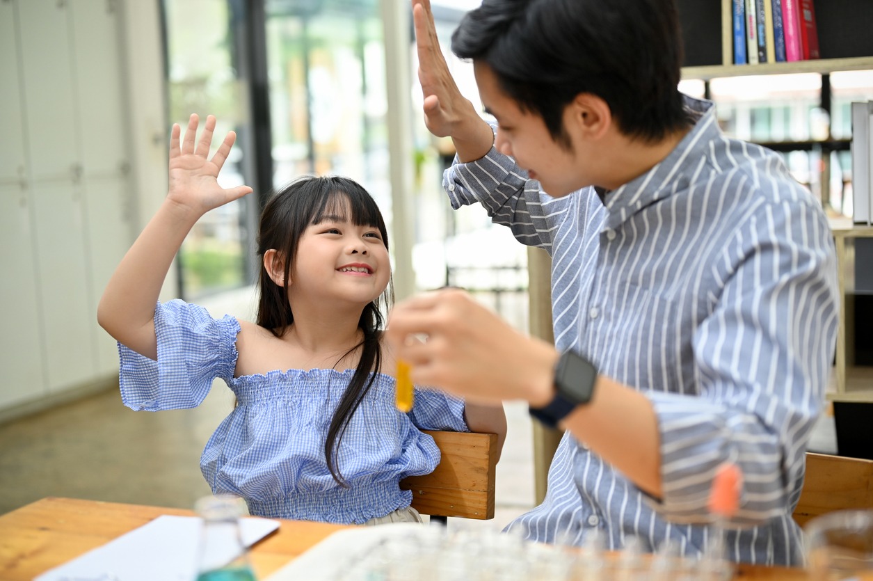 Happy proud dad or teacher giving high five to his cute little girl, doing a fun science experiment for kids. enjoying learning and doing fun activity together