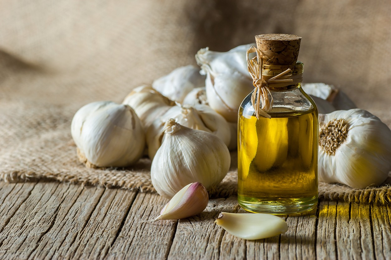 Ripe and raw garlic and garlic oil in a glass bottle on a wooden table with a burlap sack, alternative medicine, and organic cleaner. Garlic background