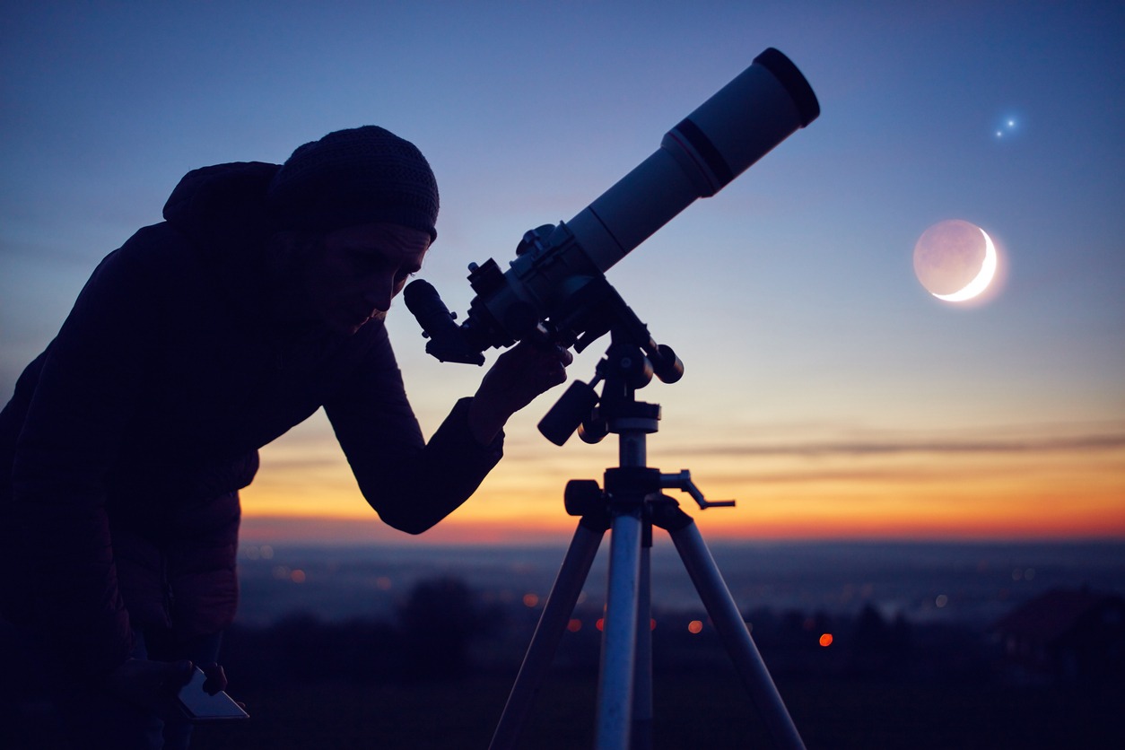 Silhouette of a woman using a telescope against the night sky.