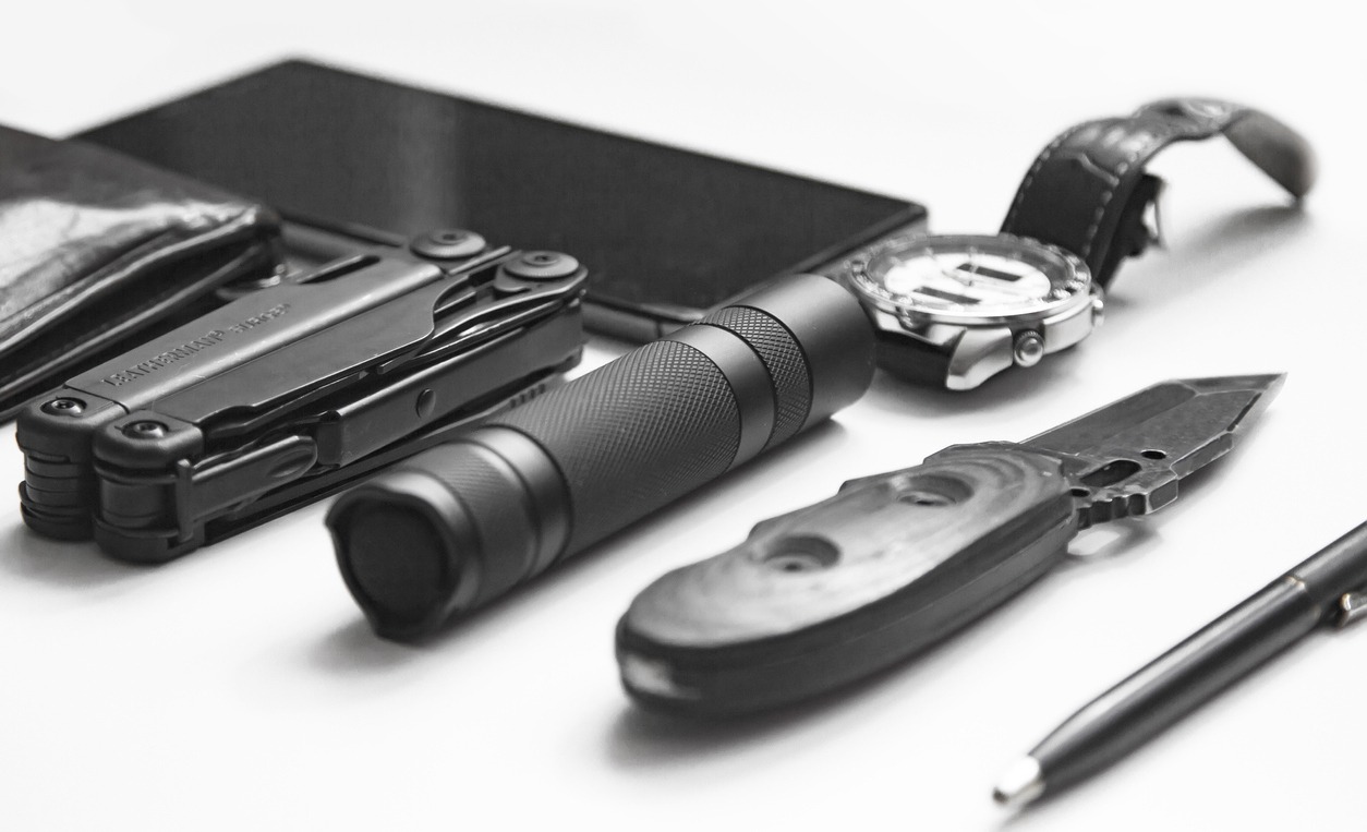 Top view of everyday carry ( EDC ) items for men in black color on white background - flashlight, watch, multi-tool multitool, phone, pen. Modern city set. Minimal concept