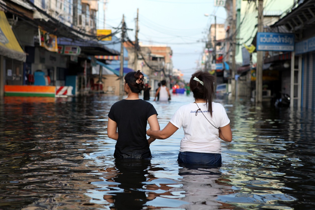 Two friends lock arms for comfort as they walk down a flooded street of Rangsit in Pathum Thani province