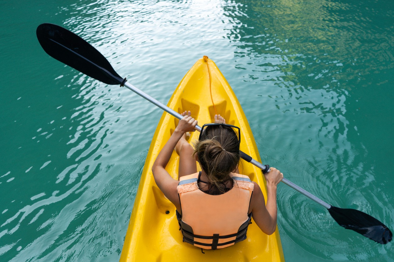 Woman paddles kayak in the lake with turquoise water.