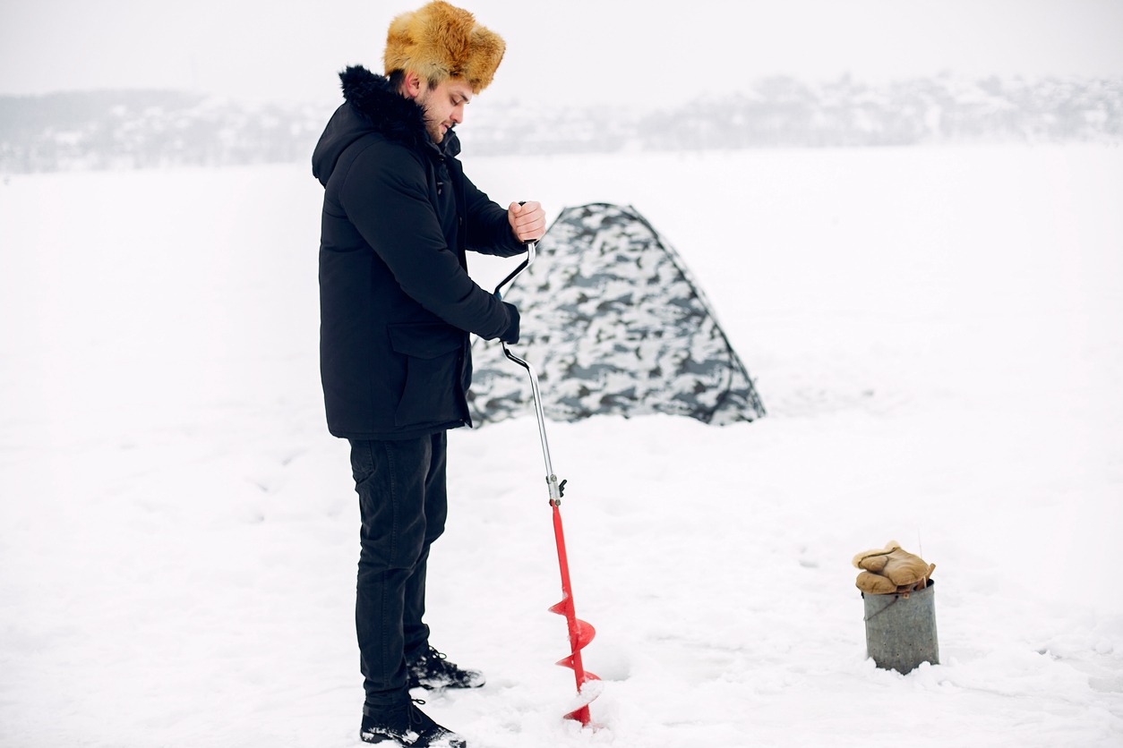 caucasian male drilling a hole with an ice auger for ice fishing