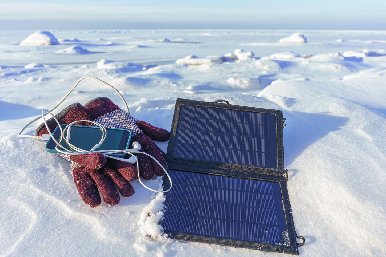 Charging mobile phone from portable tourist solar panel in winter, in cold conditions