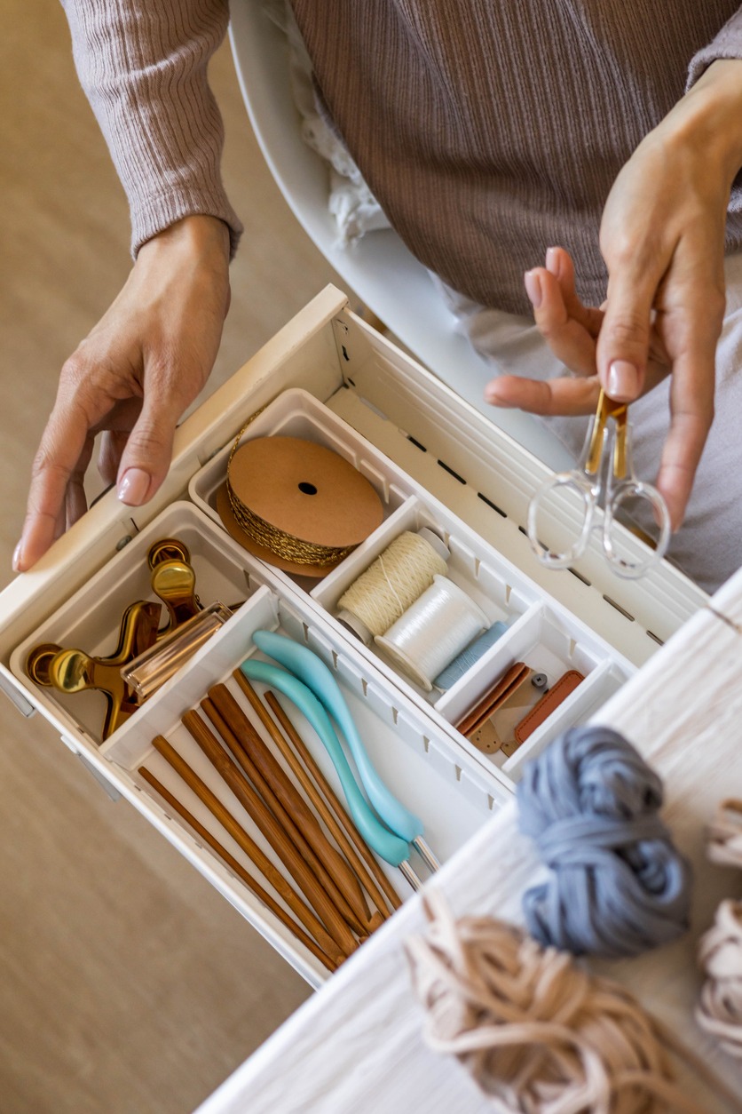 Female hands putting scissors into drawer with sewing accessories neatly placing organizing top view