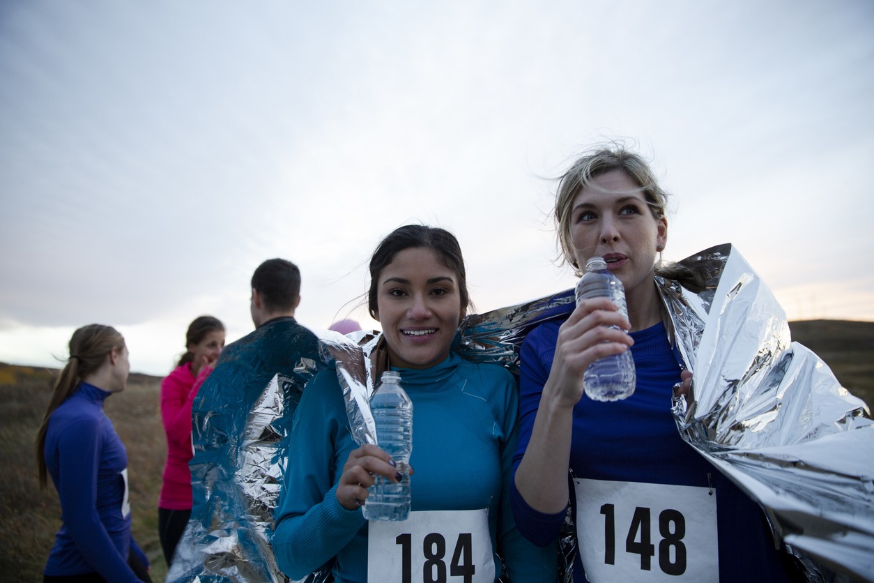 Portrait female runners in foil blanket drinking water after race