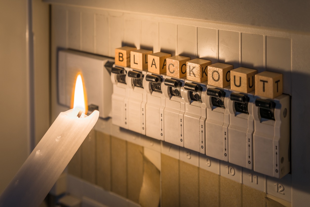 Fuse box with fuses in a distribution box during a power outage lit with white candle holding a man with the word blackout as text, Germany