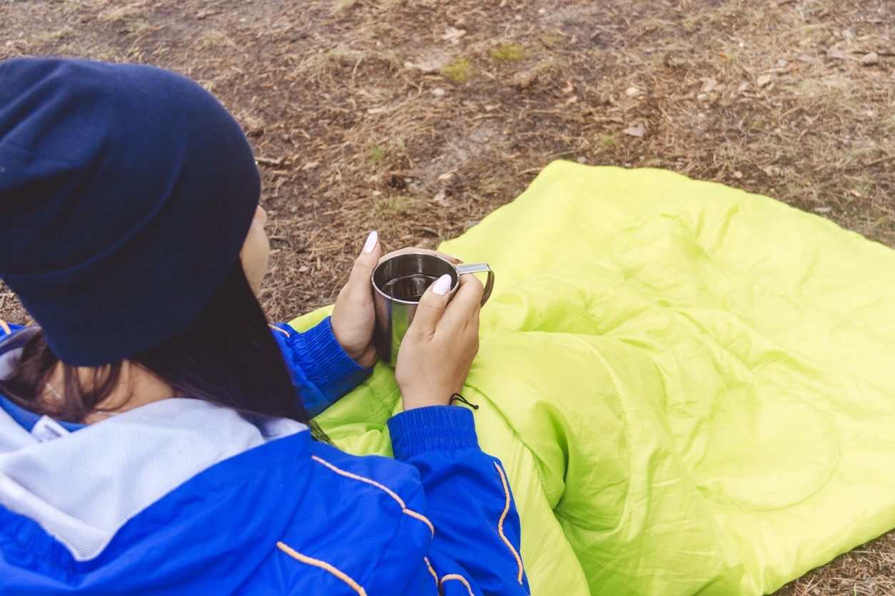 A girl in a light-green sleeping bag is drinking tea or coffee since morning. The concept of tourism and travel