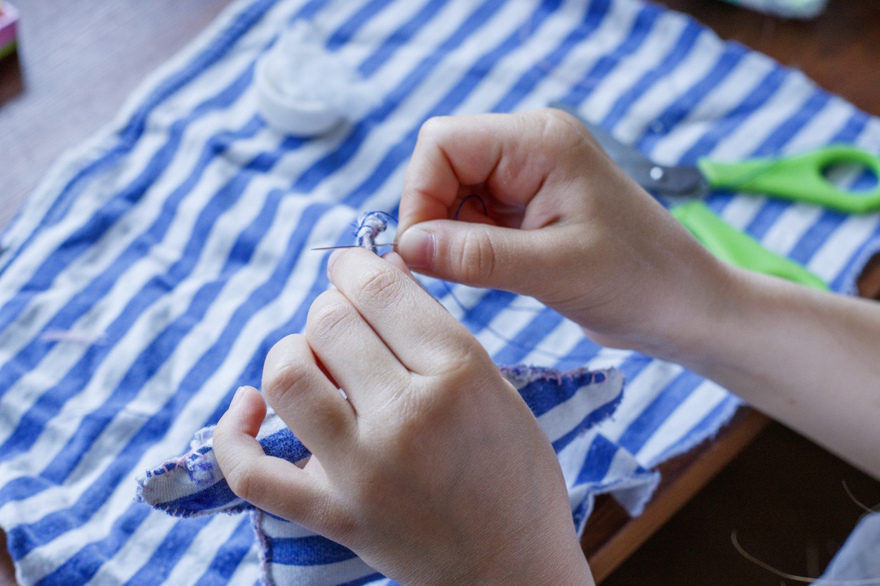 The first steps of the girl in mastering sewing. Needle with thread in the hands of the child