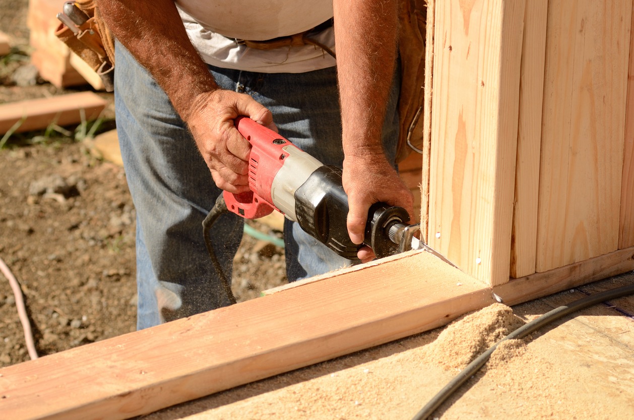worker cutting out the door in the base plate of the wall with a reciprocating saw 