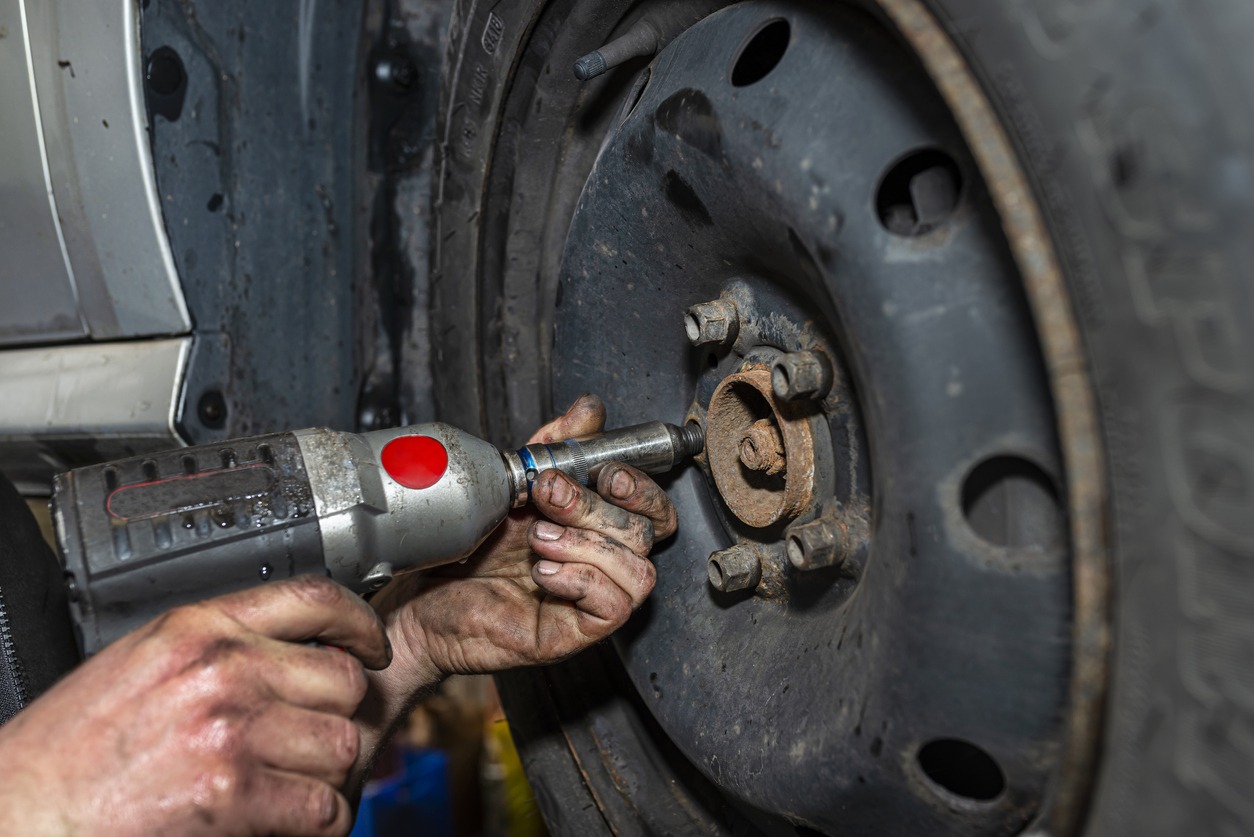 A car mechanic bolts the steel car wheel with a pneumatic wrench in a car workshop