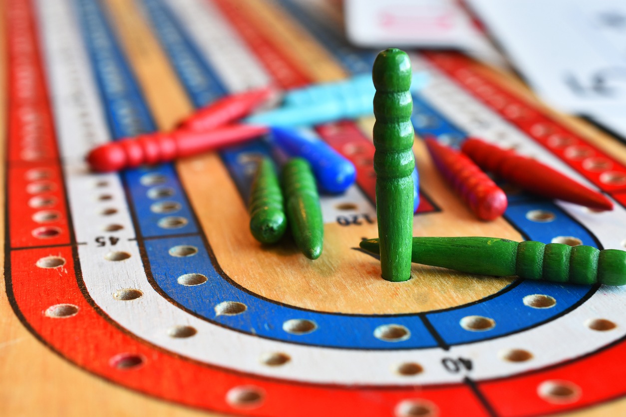 A close up image of a green cribbage pegs in the winning position on a cribbage board