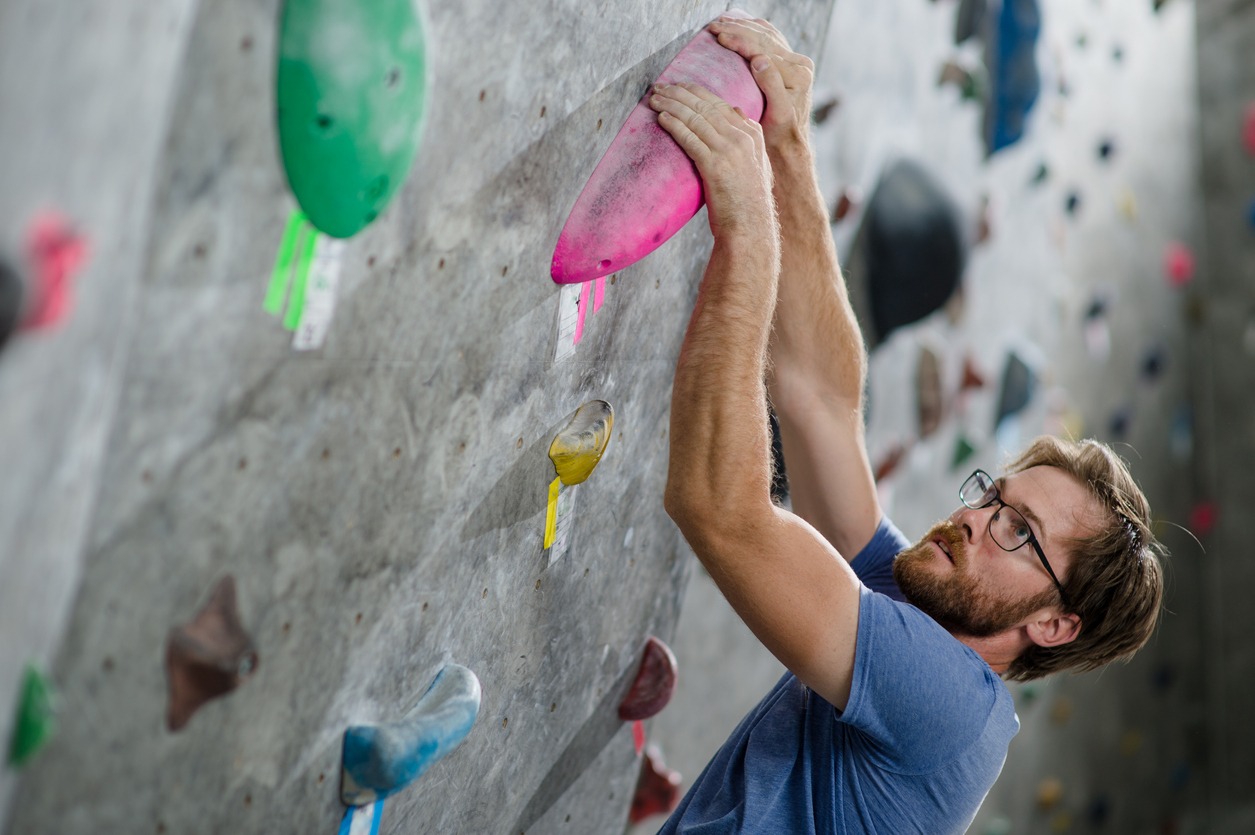 A guy rock climbing with glasses