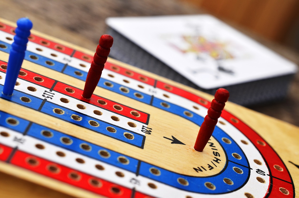 Close up image of a red, white, and blue cribbage board with the Jack of Spades card in the background