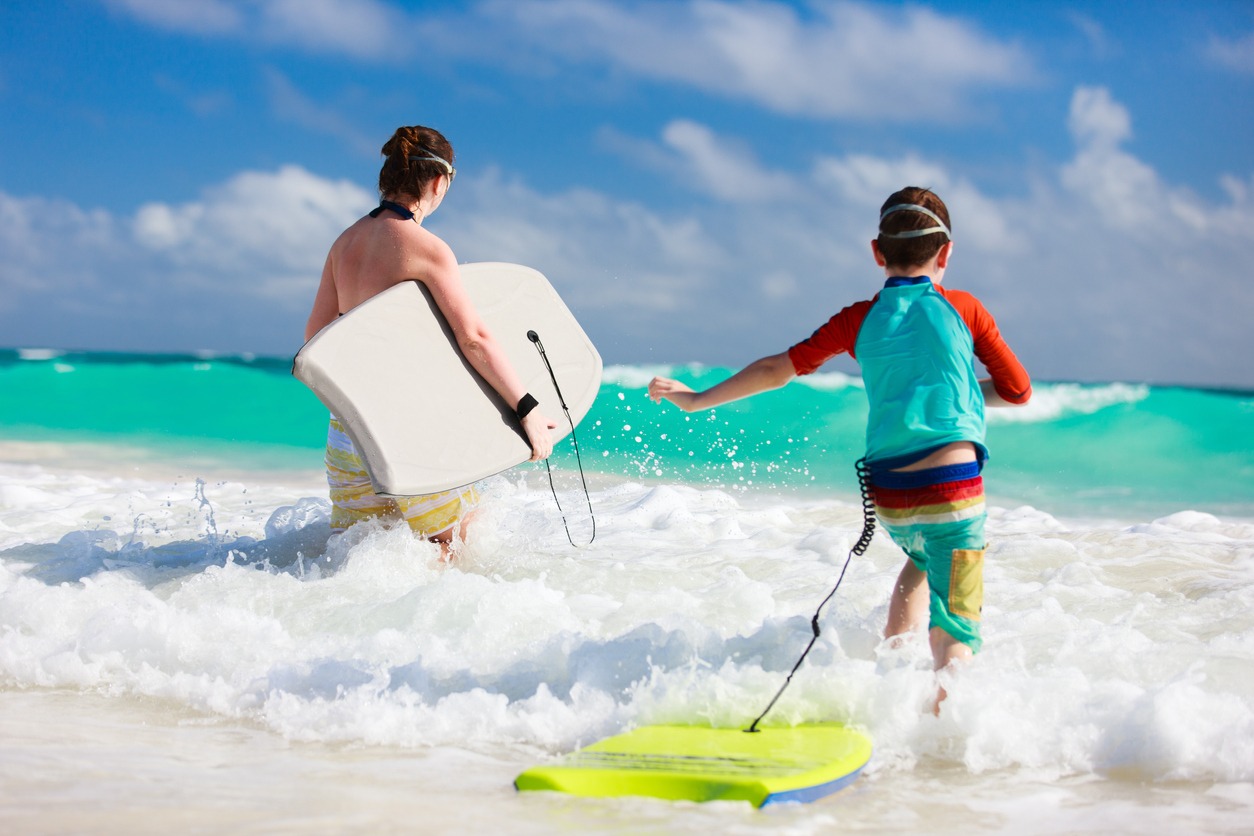Mother and son running towards ocean with boogie boards