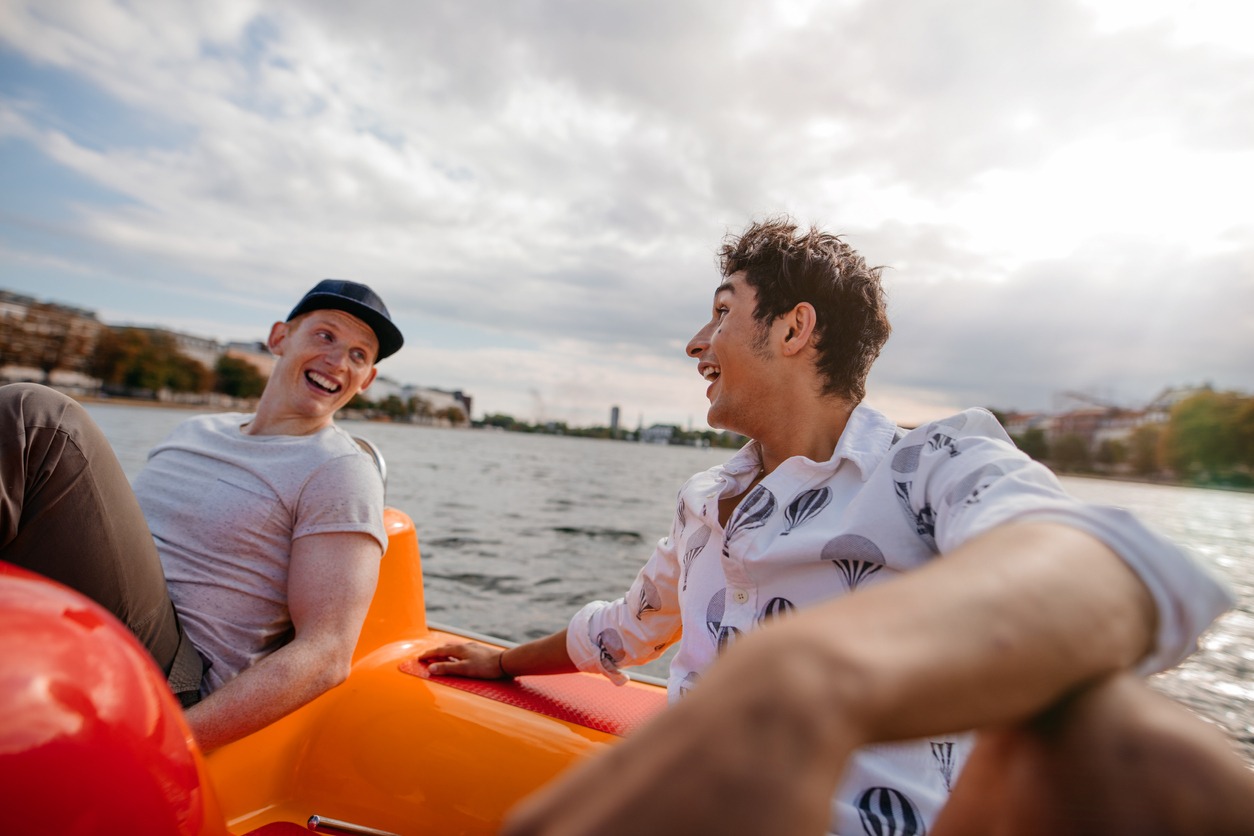 Outdoors shot of two young friends sitting in pedal boat. Teenage boys enjoying boating in the lake.