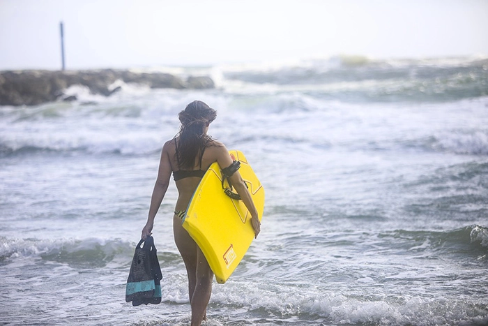 a-woman-going-to-the-ocean-while-carrying-a-bodyboard-on-a-leash-and-swim-fins