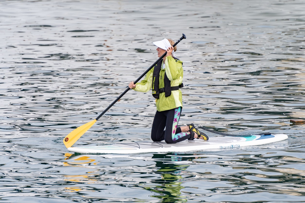a woman wearing a sun visor while standup paddle boarding