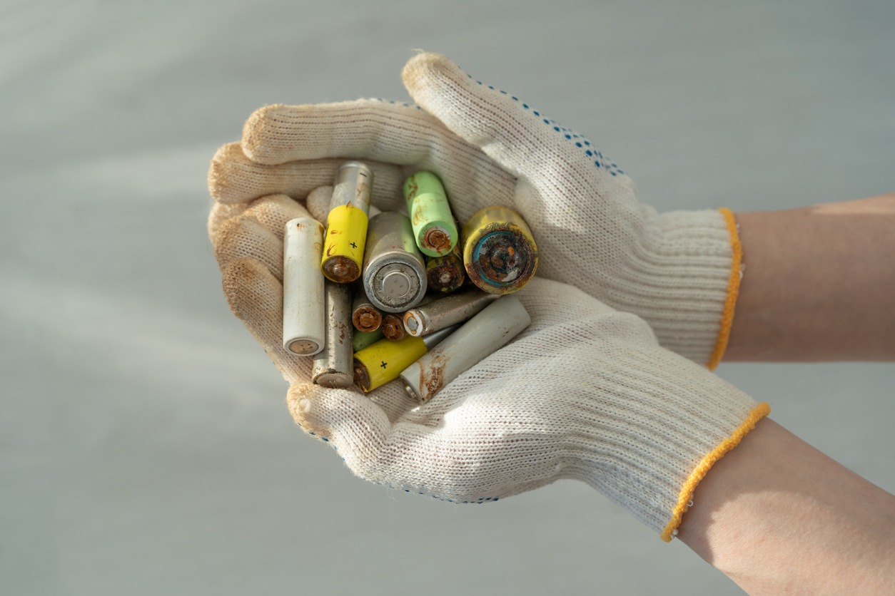 Close up of female hands in cotton protection gloves holding used alkaline batteries heap