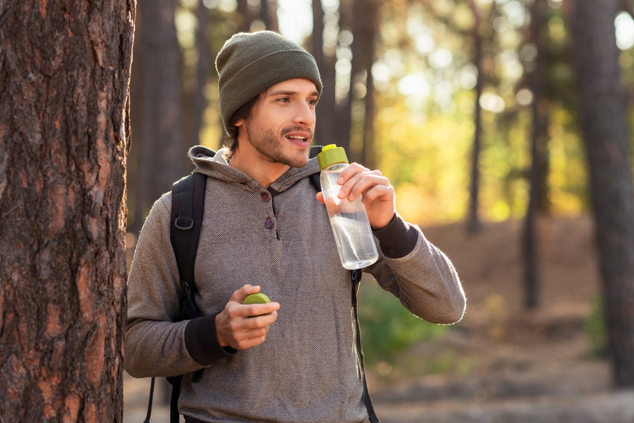 Handsome guy drinking water while walking by forest