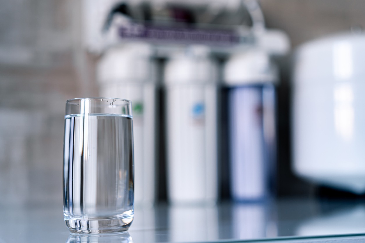 Pure water in glass and water filters on the blurred background. Household filtration system