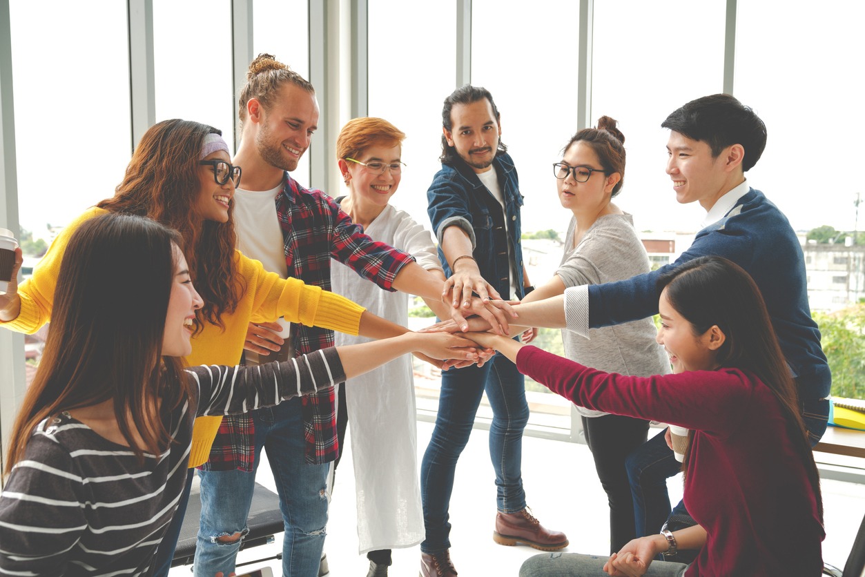 Multiethnic young team stack hands together as unity and teamwork in modern office. Diverse group togetherness collaboration or friends huddle concept. Startup business team building with soft tone