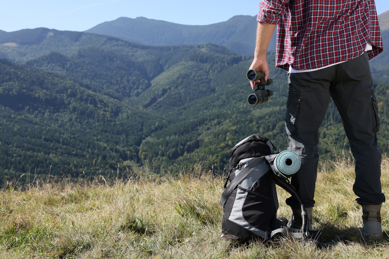 Back view of tourist with hiking equipment and binoculars in mountains