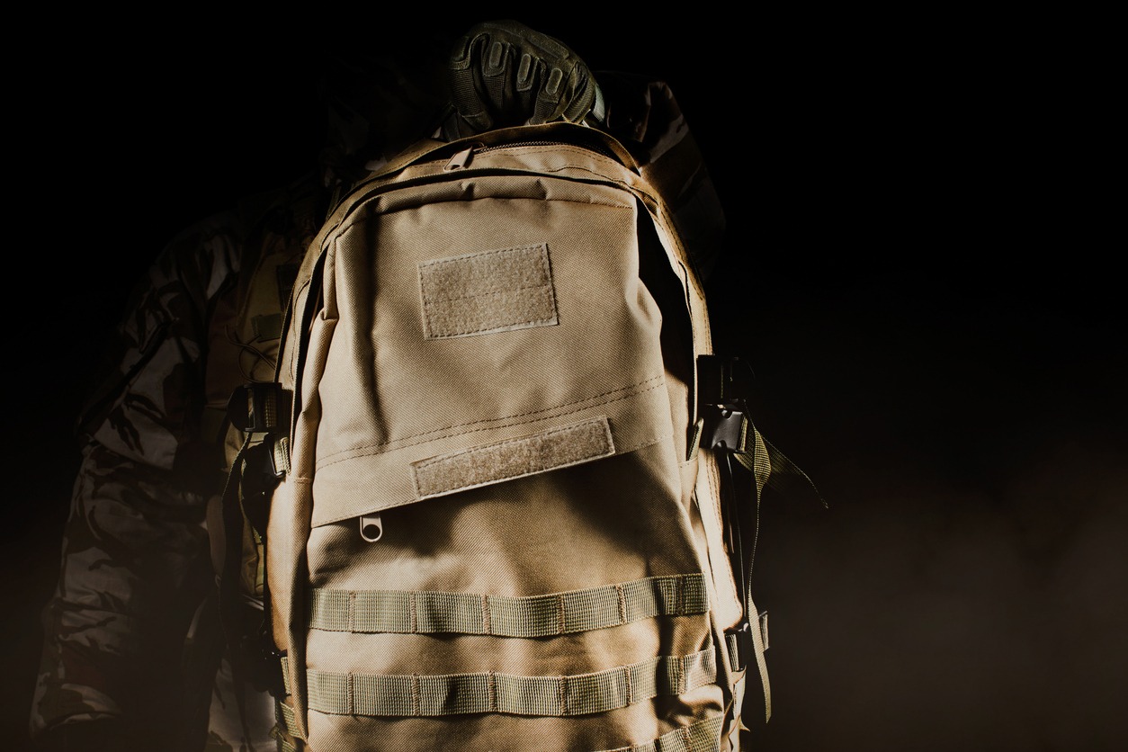 Photo of a fully equipped soldier in uniform holding backpack