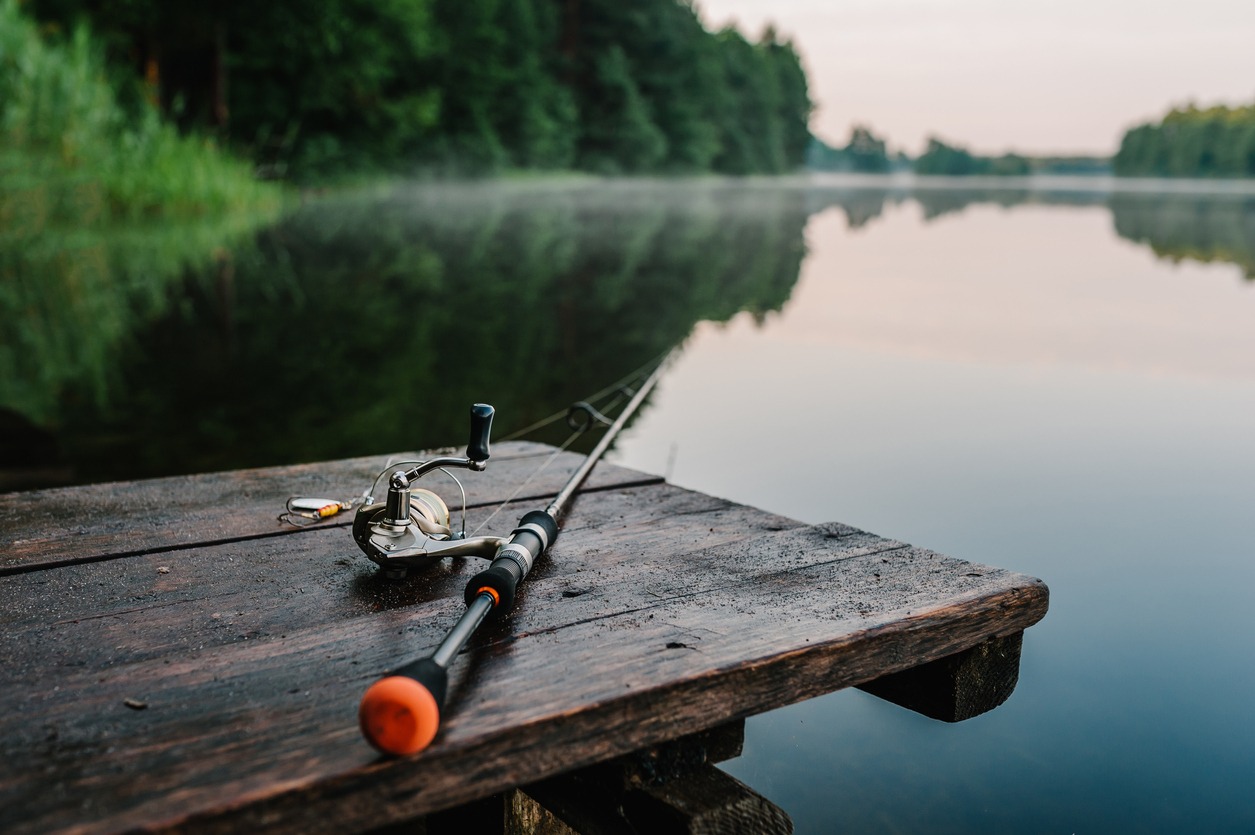 Fishing rod, spinning reel on the background pier river bank. Sunrise. Fog against the backdrop of lake. Misty morning. wild nature. The concept of rural getaway. Article about fishing day