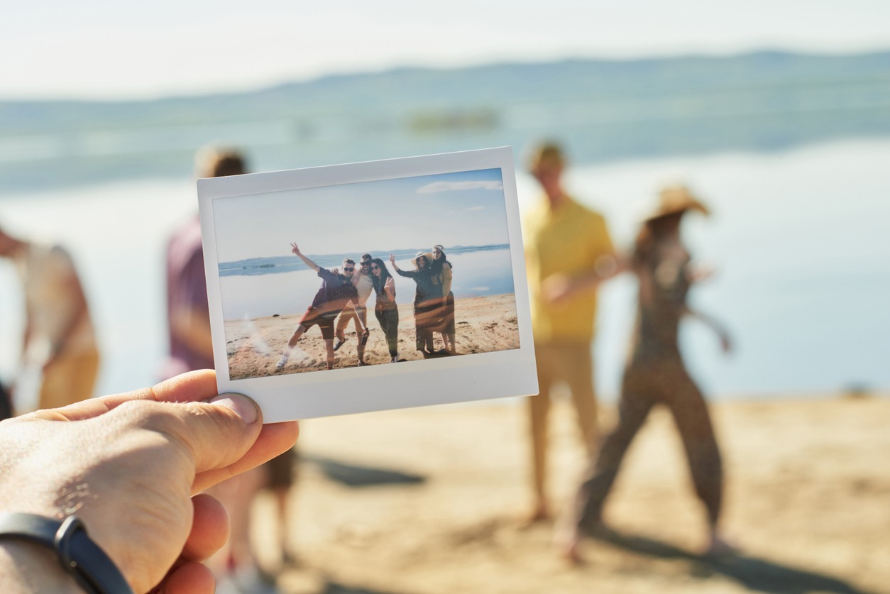 A Polaroid picture is held against a group of friends at the beach