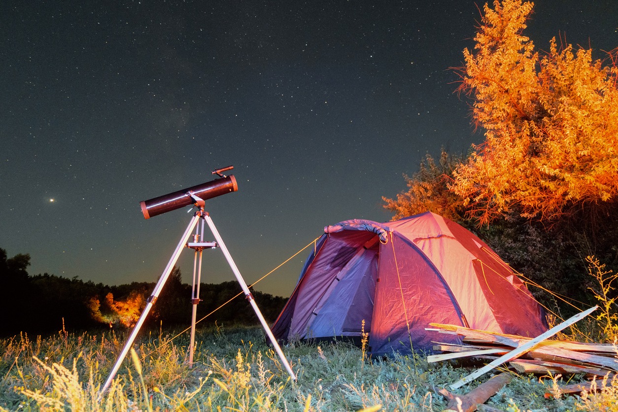A reflector telescope placed beside a camping tent