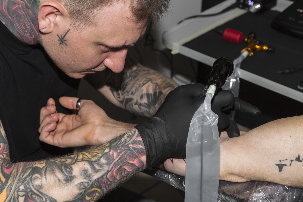 a-man-bending-over-a-mans-arm-while-making-a-tattoo-on-it
