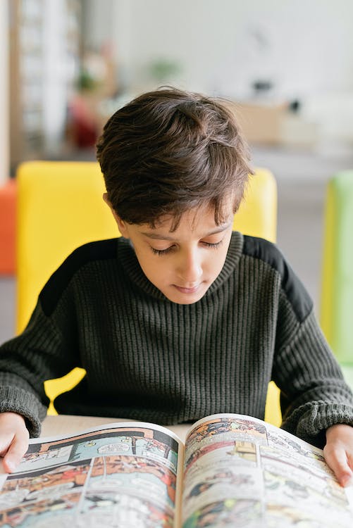 Boy in Black Sweatshirt Sitting and Reading a Comics