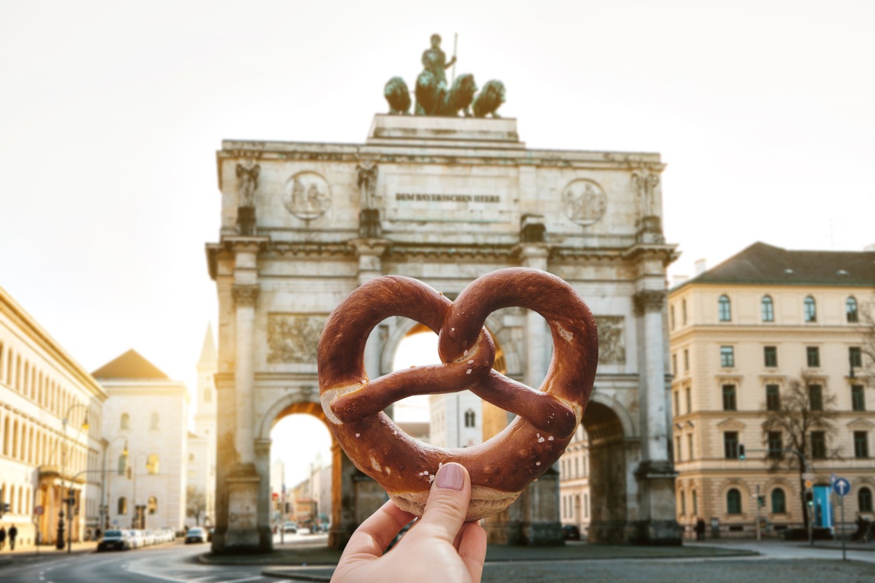 a girl holding a traditional German pretzel against the backdrop of Victory Gate triumphal arch 