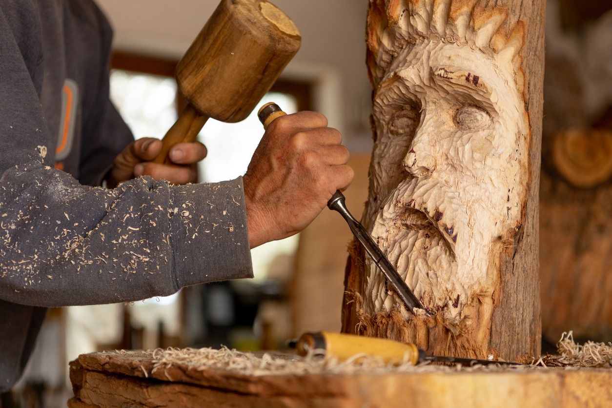 close up of artist artisan carving a wood spirit sculpture with mallet and chisel by hand in wood workshop