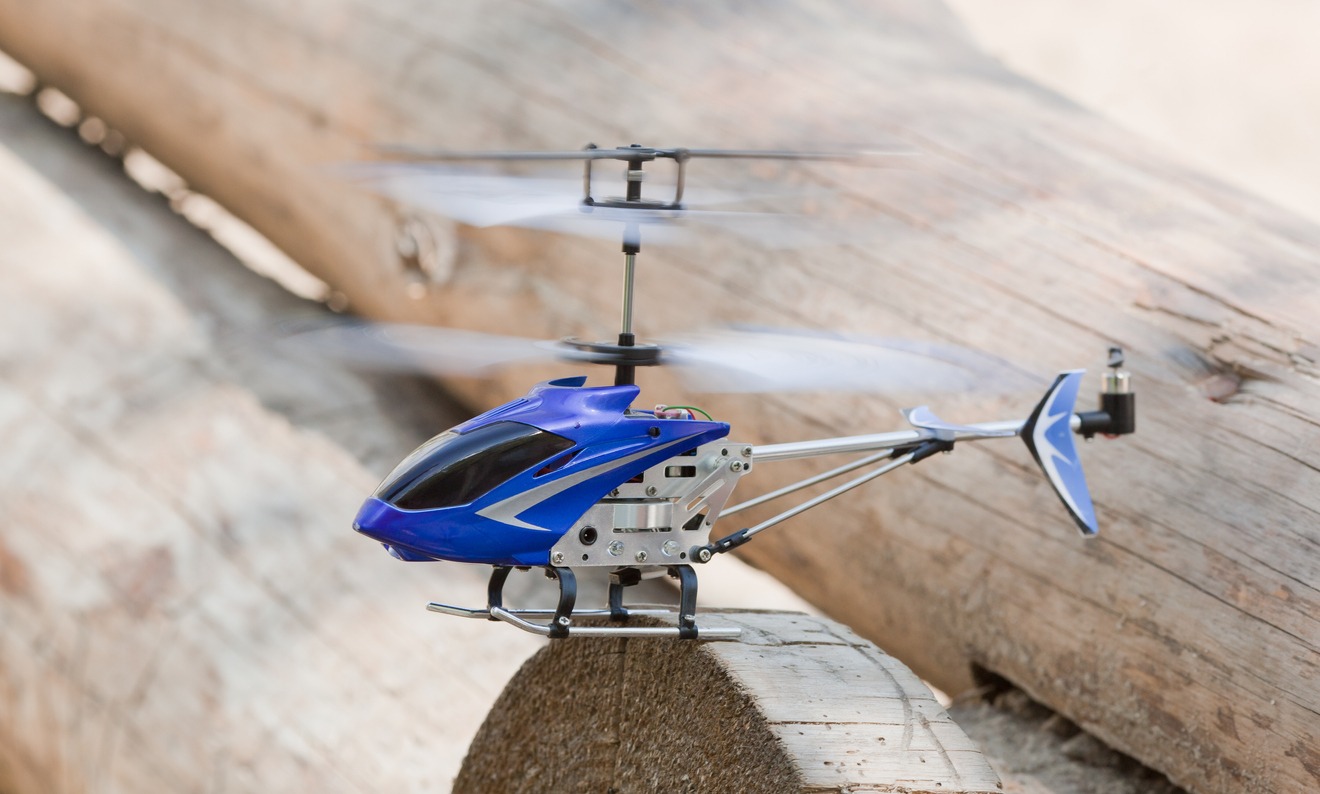 A mini RC helicopter rising over timber