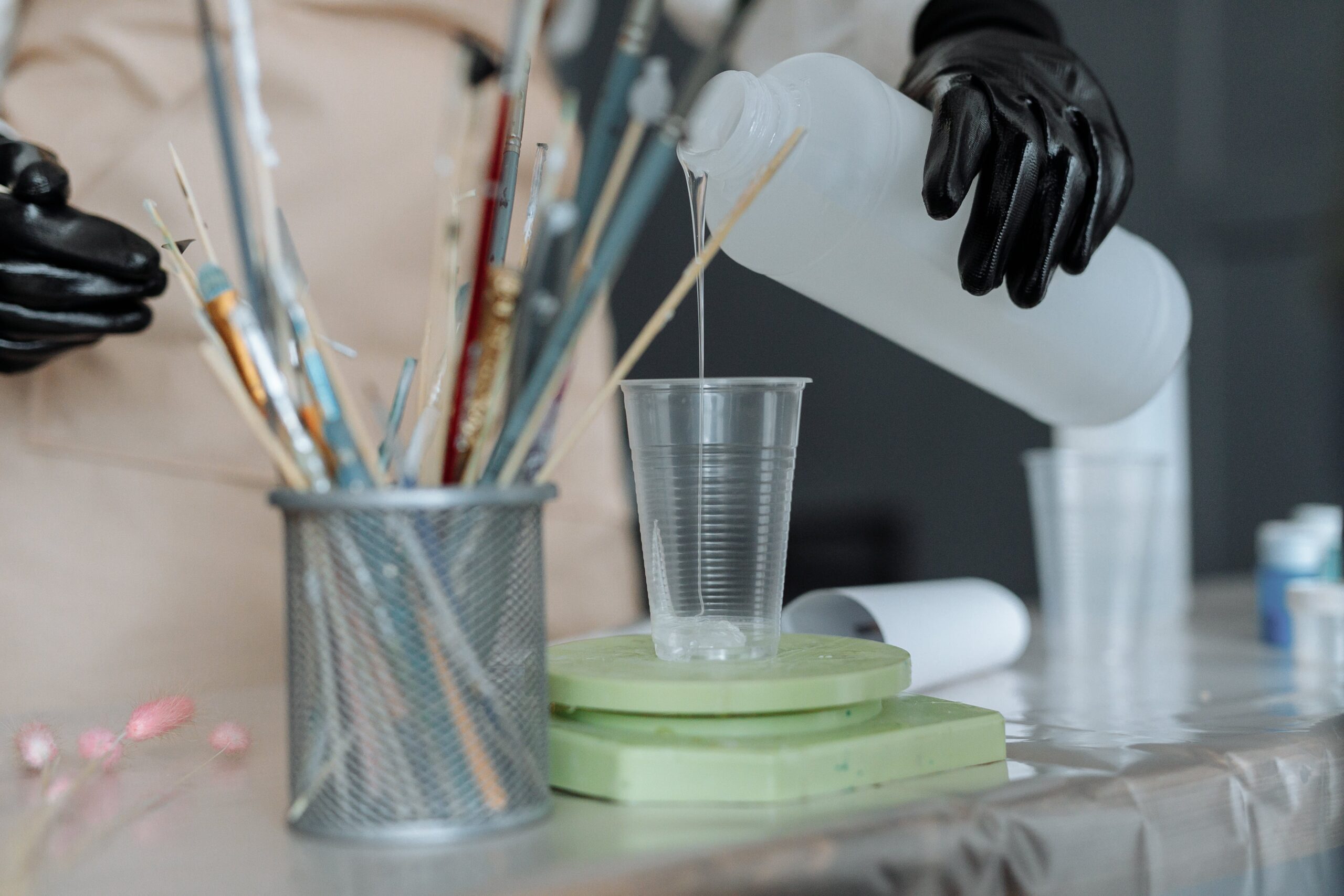 a-person-wearing-rubber-gloves-pouring-resin-on-plastic-cup