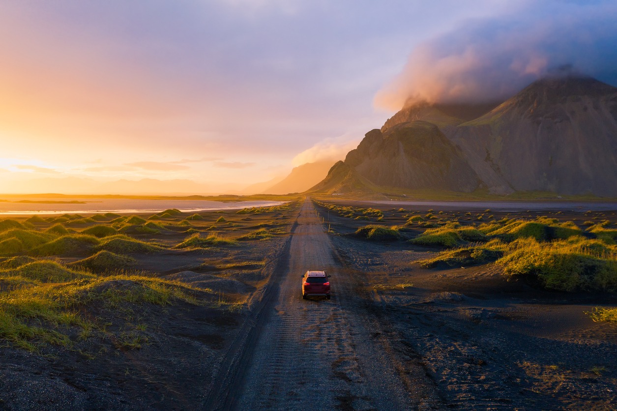 gravel-road-at-sunset-with-vestrahorn-mountain-and-a-car-driving-iceland