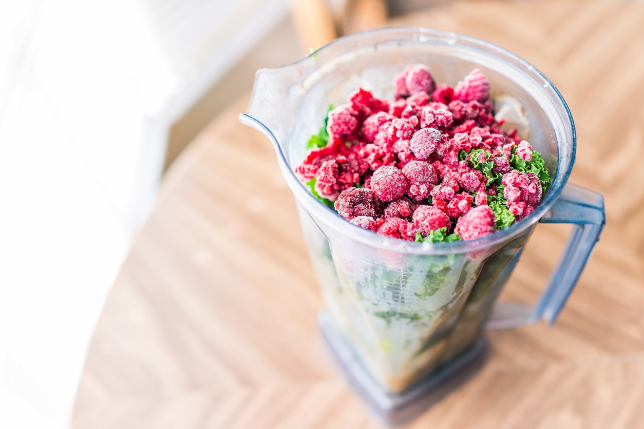 macro-closeup-of-fresh-green-kale-and-frozen-raspberries-in-plastic-blender-container