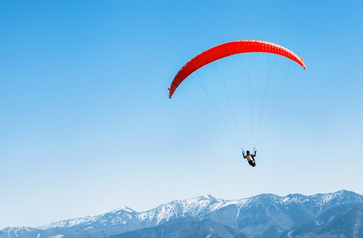 sportsman-on-red-paraglider-soaring-over-the-snowy-mountain-peaks
