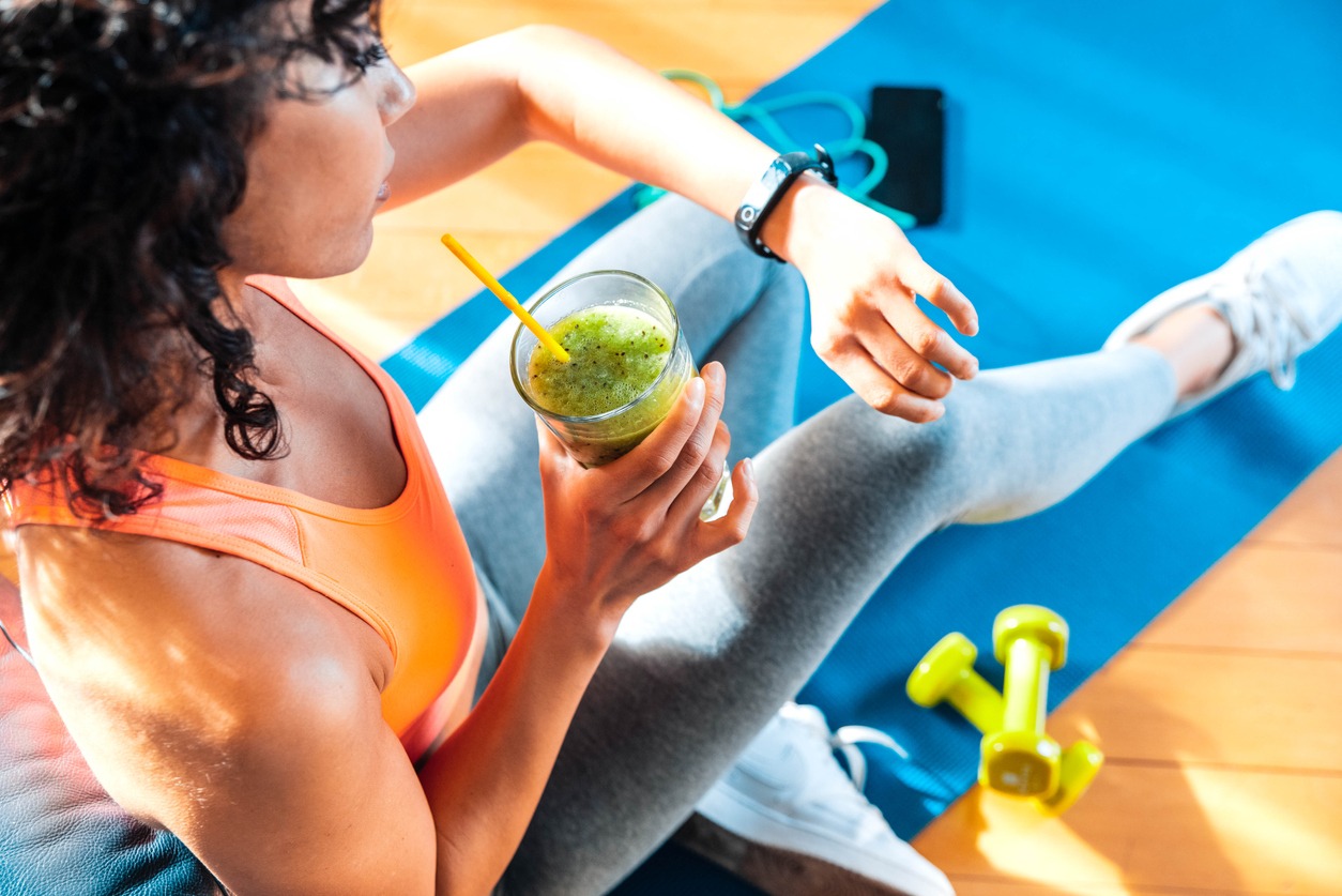 sporty-woman-in-sportswear-training-at-home-drinking-fresh-smoothie-fit-female