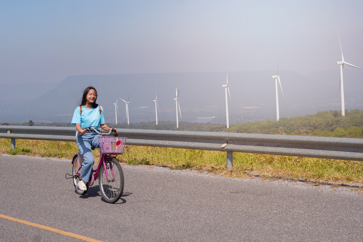 young-girl-ride-a-bike-on-the-road-at-the-mountain-with-wind-turbine