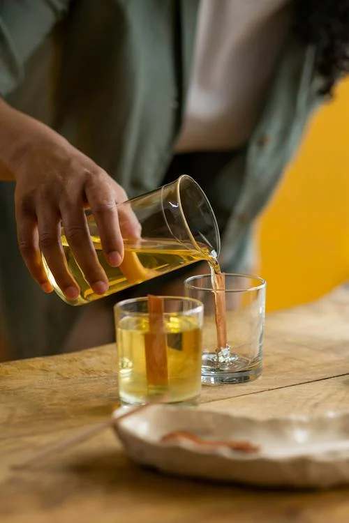 Person pouring yellow liquid in clear glass